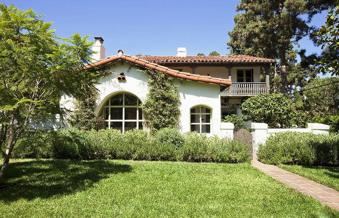 A white, one-story Spanish Colonial Revival house with a red tile roof, arched windows, and a lush green lawn.