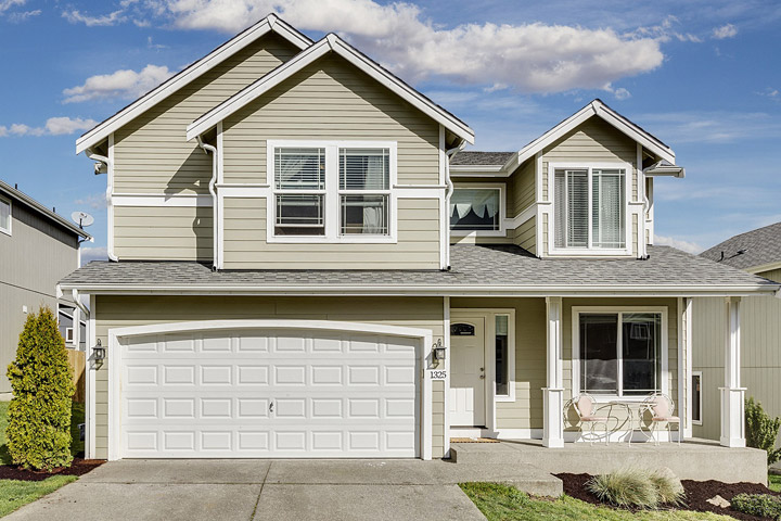 Two-story suburban house with light beige siding, white trim, and a large garage, featuring a front porch